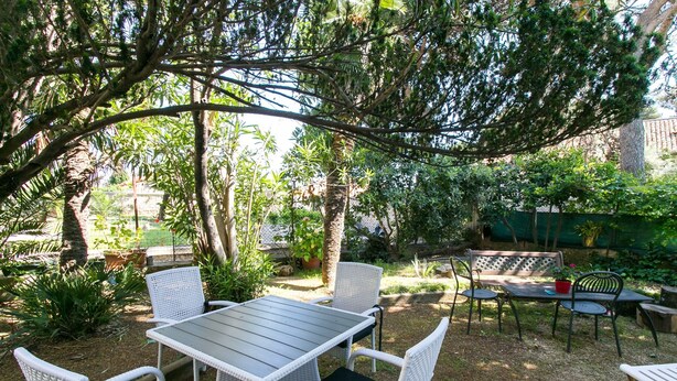 Une terrasse extérieure avec une table et des chaises, entourée de verdure et d’arbres.