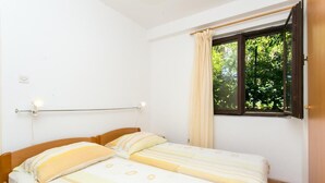 Une petite chambre propre, avec deux lits simples, une fenêtre avec des rideaux et un plancher en bois.