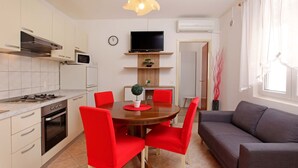 Cocina compacta con comedor, un sofá gris y un televisor en la pared.