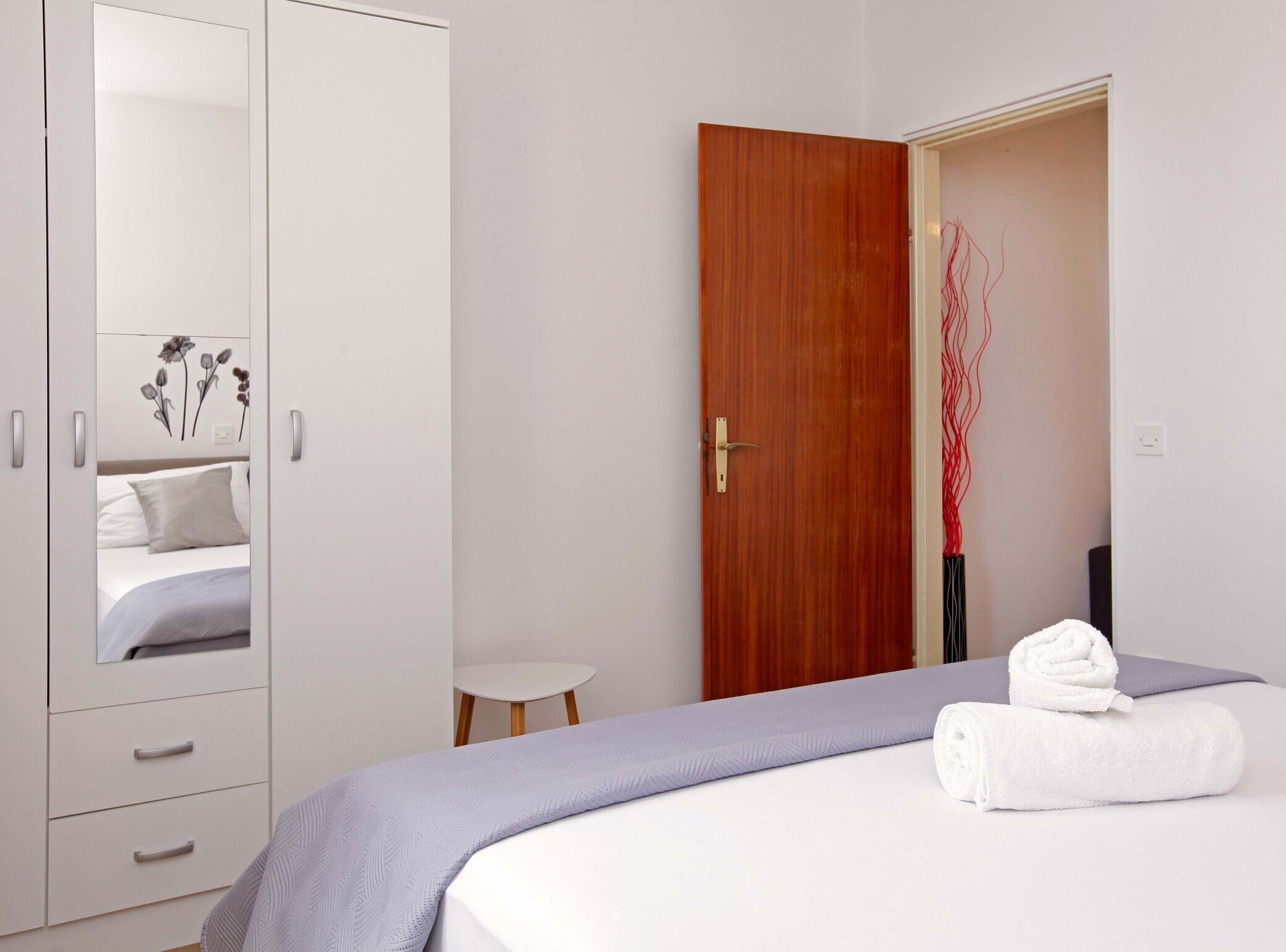 A bedroom with a bed, a wardrobe, a small table, and a door.