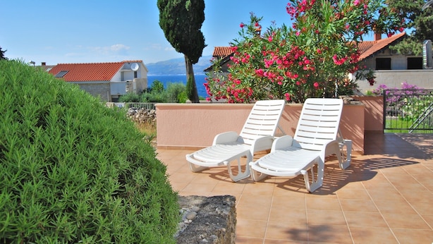 Eine Terrasse mit zwei weißen Liegestühlen, einem großen Busch und Blick aufs Meer.