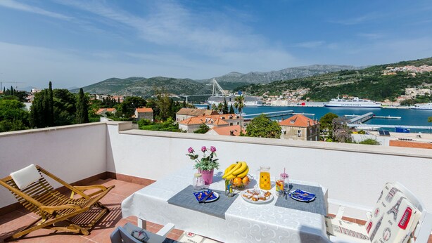 Eine Terrasse mit Frühstückstisch, mit Blick auf einen Hafen, eine Brücke, Berge und eine Küstenstadt.