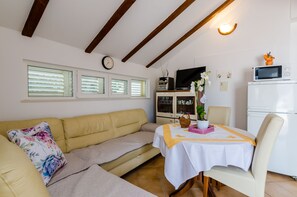 A cozy living room with a sofa, a dining table with a white tablecloth, a television, and a refrigerator.