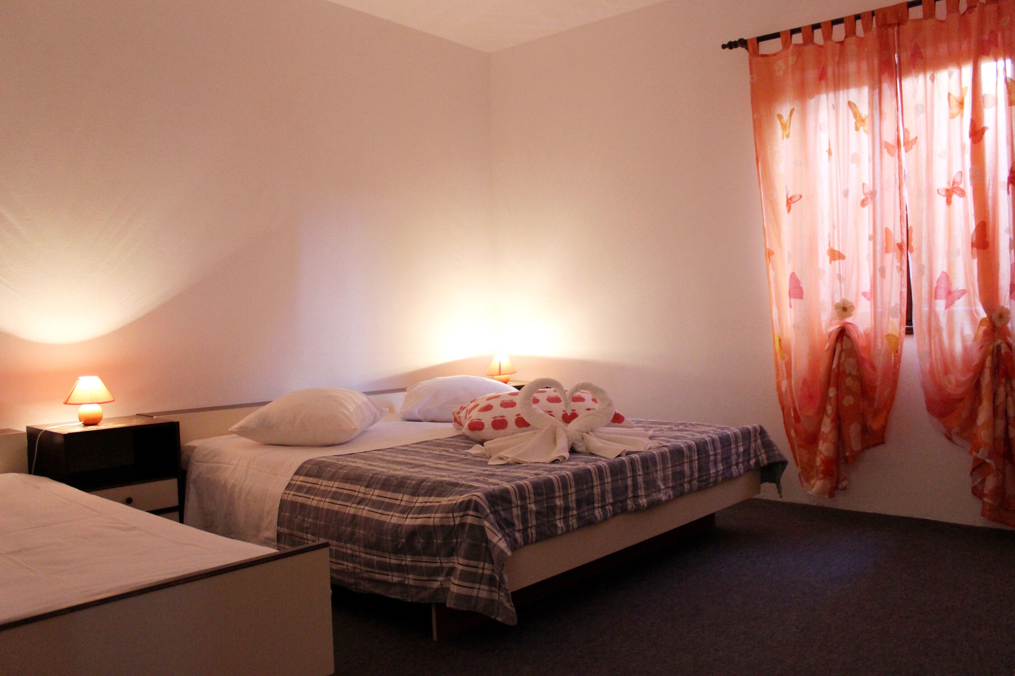 A bedroom with a bed, two bedside tables, a lamp, and a window with curtains.