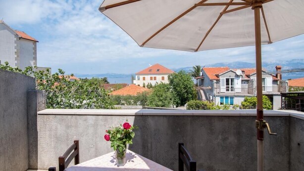 Una terraza con mesa y sillas, un paraguas blanco y vistas a edificios y montañas al fondo.