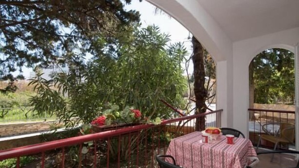 An outdoor balcony with a table set for two, surrounded by greenery and a red railing. - Apartments Boguvila - Two-Bedroom Standard Apartment with Terrace (Supetar)