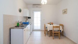 A compact kitchen with a dining area, a white refrigerator, a sink, and a table set for two. - Apartments Boguvila - Two-Bedroom Standard Apartment with Terrace (Supetar)