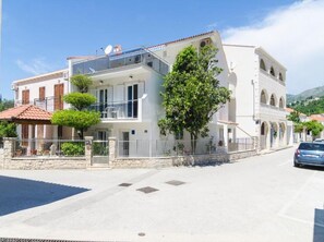 Un immeuble de deux étages doté de balcons, d’un mur en pierre et d’une voiture garée.