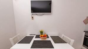 A dining table with four chairs, a flat-screen TV mounted above, and a basket of fruit on the table. - Apartments Magdalena - Apartment with Sea View and Terrace (A3) (Bol)