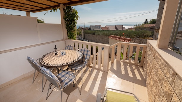 A covered outdoor patio with a round table and chairs, a view of the sea, and a stone wall. - Apartments Magdalena - Apartment with Sea View and Terrace (A3) (Bol)