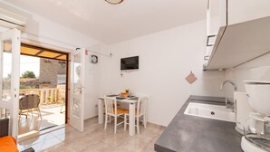 A compact kitchen with a dining area, a TV mounted on the wall, and a view of the outside balcony. - Apartments Magdalena - Apartment with Sea View and Terrace (A3) (Bol)