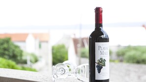 A bottle of Plavac Mali wine and a broken glass on a balcony railing with a view of buildings and greenery in the background. - Apartments Magdalena - Apartment with Sea View and Terrace (A3) (Bol)