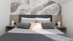 Une chambre à coucher moderne avec un grand lit, une tête de lit ornée d’un motif géométrique et une fresque murale aux motifs abstraits.