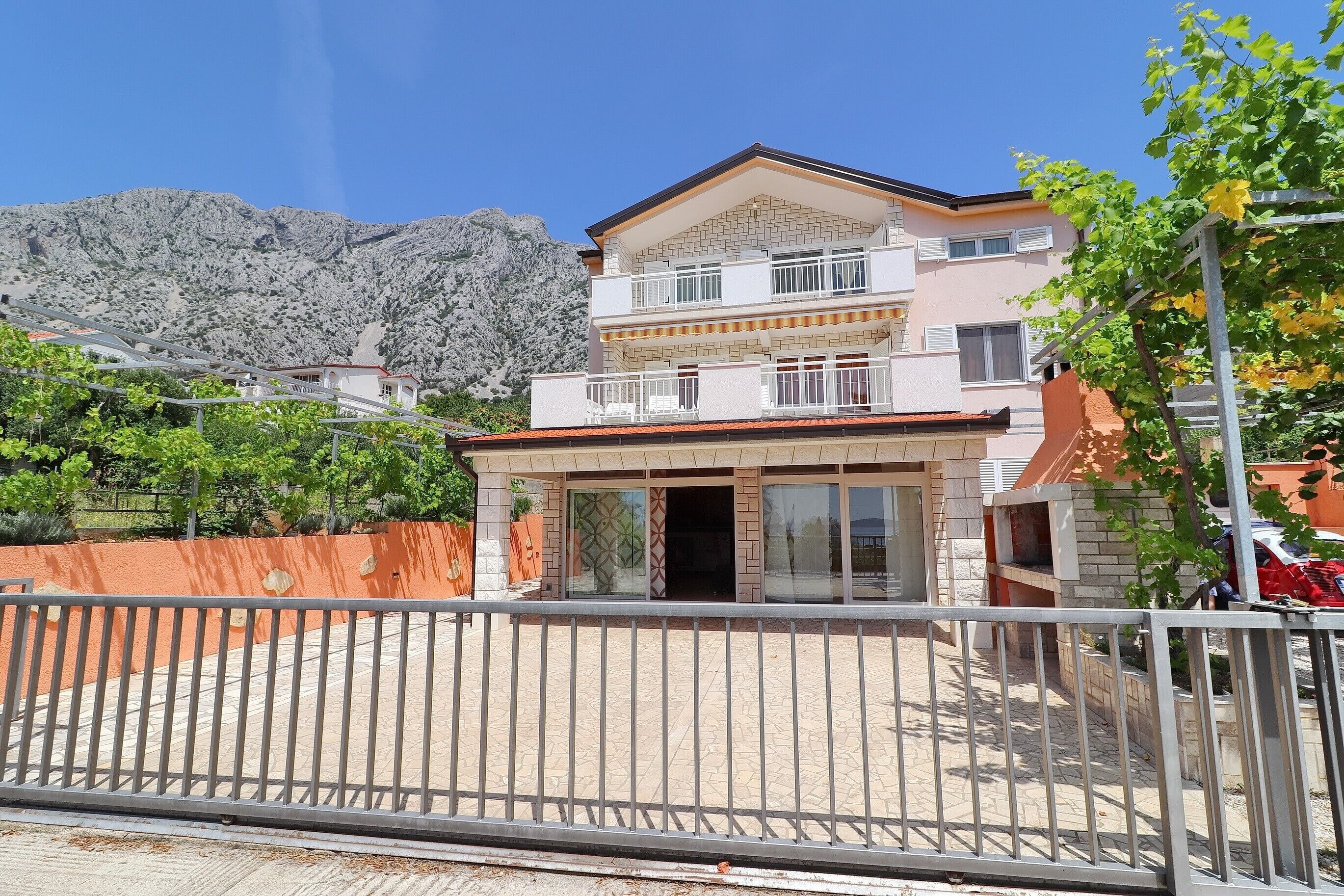 A two-story building with a balcony, a paved driveway, and a mountain in the background.