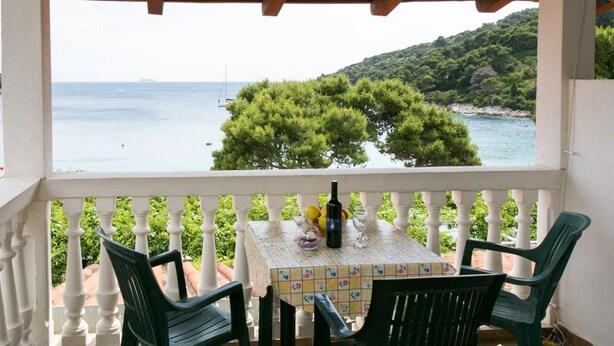 Un balcon avec une table et des chaises, offrant une vue sur la côte, avec des arbres et la mer.