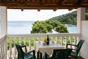 A balcony with a table and chairs, overlooking a coastal view with trees and the sea.