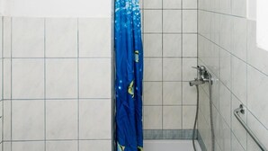 Un petit espace de douche carrelé, avec un rideau de douche bleu, une douchette à main et une serviette blanche sur le sol.