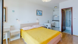 Una camera da letto con un letto, un comodino e una piccola scrivania. È presente anche un angolo cottura con lavandino e una sedia.