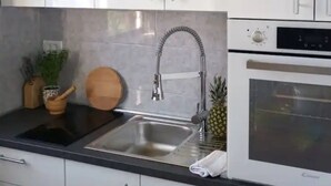 A kitchen with a stainless steel sink, a wooden cutting board, a pineapple, and a white oven. - Apartments Natasa- One Bedroom Apartment with Balcony (Supetar)