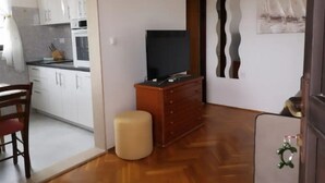 A compact living space with a kitchenette, a television on a wooden dresser, a small ottoman, and a door with a decorative keychain. - Apartments Natasa- One Bedroom Apartment with Balcony (Supetar)