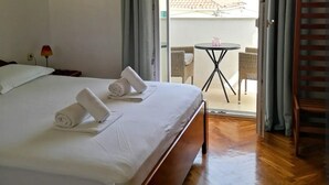 A hotel room with a neatly made bed, a small balcony table, and wicker chairs. - Apartments Natasa- One Bedroom Apartment with Balcony (Supetar)