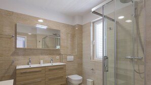 Ein modernes Badezimmer mit Duschkabine aus Glas, einem großen Spiegel und einem Holzwaschtisch mit Waschbecken und Toilette.