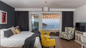 Ein modernes Hotelzimmer mit einem großen Bett, einem Fernseher, einer Sitzecke und einem Balkon mit Meerblick.