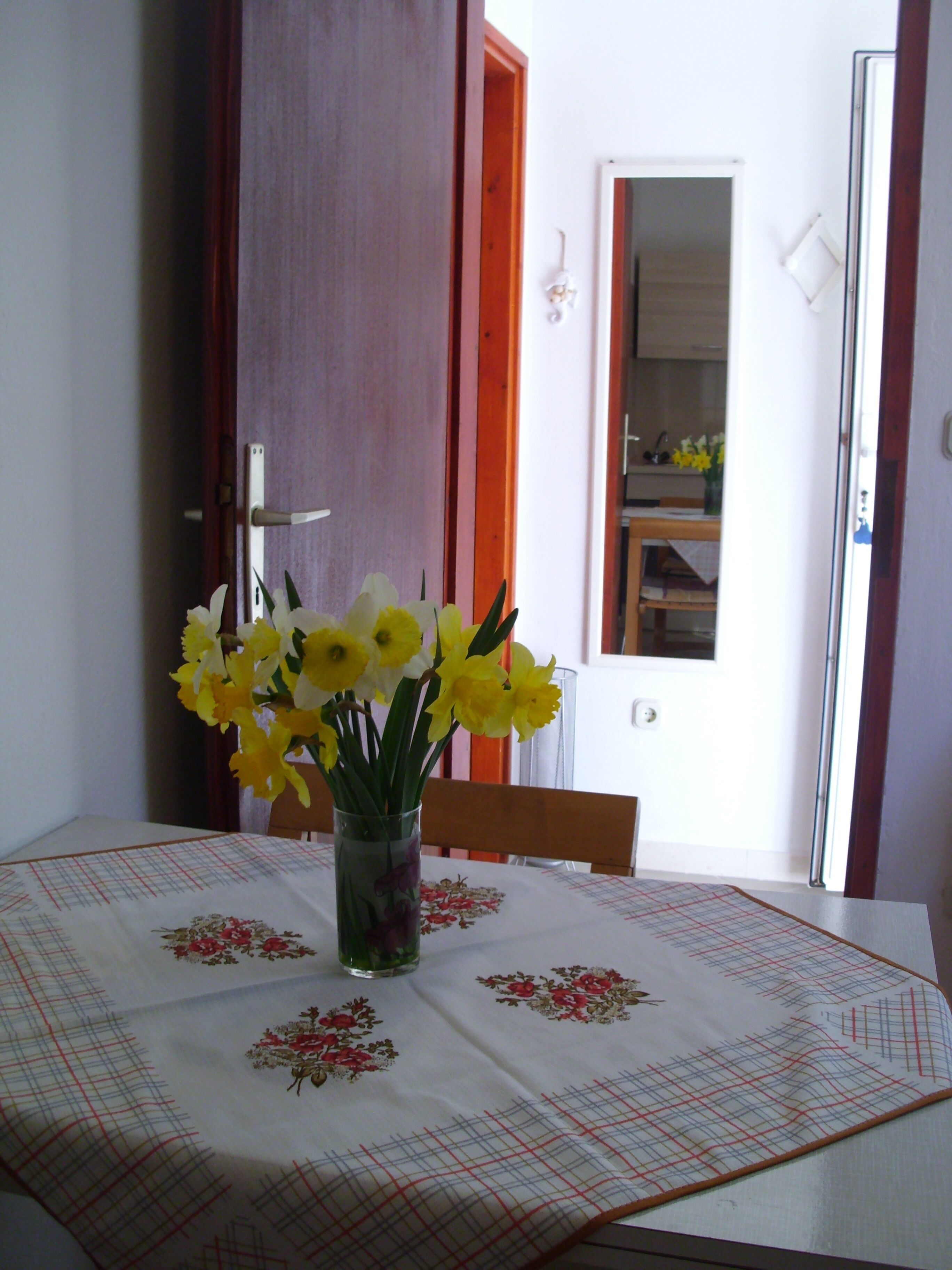 Une table à manger recouverte d’une nappe à motifs floraux et ornée d’un vase contenant des fleurs jaunes et blanches.
