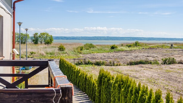 A view from a balcony overlooking a beach with a wooden deck and a row of evergreen shrubs. - Apartamenty Sun & Snow Niska (Krynica Morska)