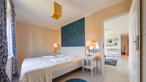 A bedroom with a bed, bedside tables, a desk, a chair, a blue rug, and a large wall painting. - Apartamenty Sun & Snow Niska (Krynica Morska)