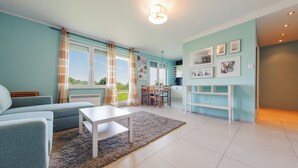 A modern living room with a sofa, a dining table, and a kitchen area with a white cabinet. - Apartamenty Sun & Snow Niska (Krynica Morska)