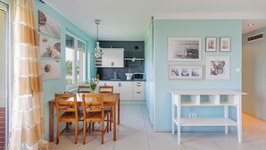 A modern kitchen with white cabinets, a dining area with wooden chairs, and a white table. - Apartamenty Sun & Snow Niska (Krynica Morska)