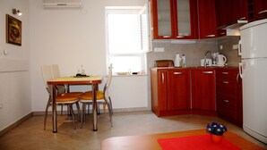 Une cuisine compacte avec des meubles en bois, un réfrigérateur blanc, une table à manger avec des chaises et une fenêtre qui laisse entrer la lumière naturelle.