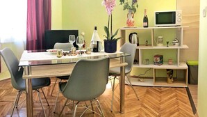 Ein Essbereich mit Glastisch, Metallstühlen, einem Blumentopf, einer Weinflasche und einer Mikrowelle auf einem Regal.