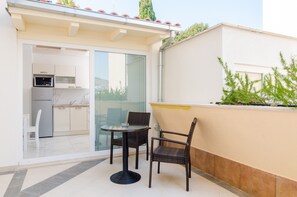 A small outdoor dining area with a table and two chairs, a sliding glass door leading to a kitchen, and a white exterior wall. - Apartment Riki - Studio Apartment with Balcony and City View (Dubrovnik)