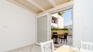 A balcony with a table and chairs, a sliding door, and a view of a building with plants and clothes hanging. - Apartment Riki - Studio Apartment with Balcony and City View (Dubrovnik)