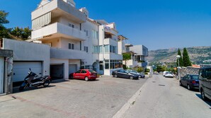 A residential street with parked cars and a building with multiple balconies and a garage. - Apartment Riki - Studio Apartment with Balcony and City View (Dubrovnik)
