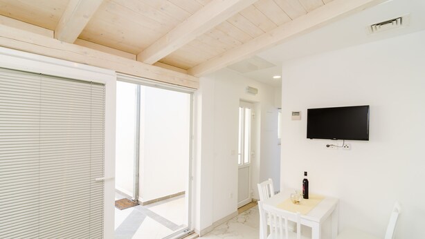 A room with a sliding glass door leading to a balcony, a flat-screen TV mounted on the wall, and a small table with a bottle and glass. - Apartment Riki - Studio Apartment with Balcony and City View (Dubrovnik)
