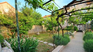 A garden with a pergola, stone wall, and a pathway leading to a gate.