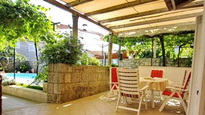 A covered patio area with tiled flooring, a stone wall, and a view of a swimming pool.