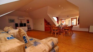 A spacious loft with a high ceiling, a dining area with wooden chairs, and a sofa with patterned cushions.
