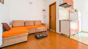 A living room with a sofa, a small table, and a kitchen area with a refrigerator and cabinets.