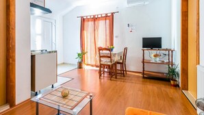 A compact living space with a kitchenette, a dining area with a table and chairs, a television on a stand, and a potted plant.