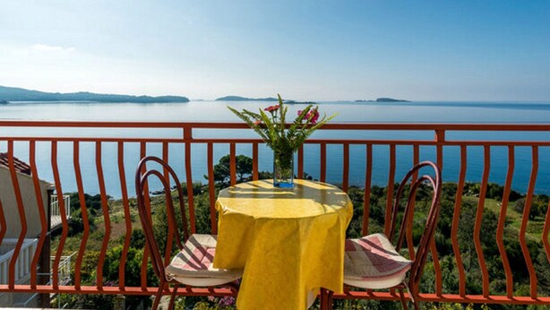 A balcony with a table and chairs, overlooking a calm sea and distant hills.
