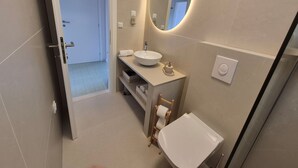 Un baño moderno con un espejo redondo, un lavabo blanco y una silla de madera.