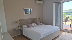 Un dormitorio con cama, mesitas de noche, aire acondicionado instalado en la pared y un ventanal con vistas.