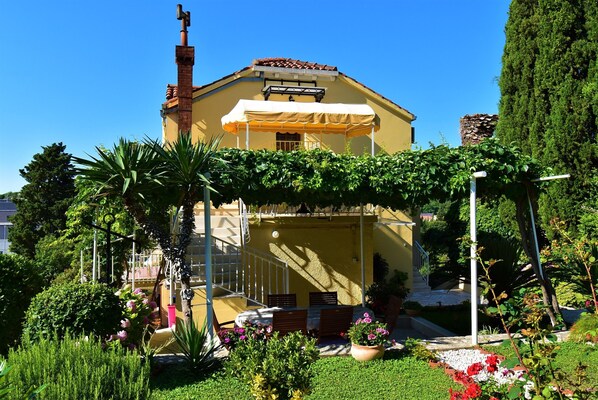 A yellow building with a covered patio, surrounded by lush greenery and a clear blue sky.
