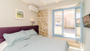 Ein Schlafzimmer mit einem Bett, einer Steinwand, einer Klimaanlage, einem gerahmten Bild und einer Schiebetür zu einem Außenbereich.