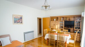 Una sala de estar con un sofá, una mesa de comedor con sillas, un televisor y un aparador con puertas de vidrio.