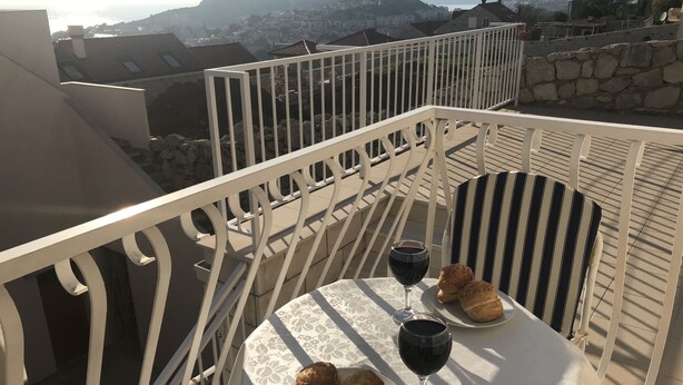 Un balcón con una mesa dispuesta para dos personas, con una copa de vino y pasteles.
